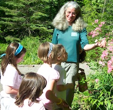 An instructor showing a blooming plant to a group of
        children in the garden
